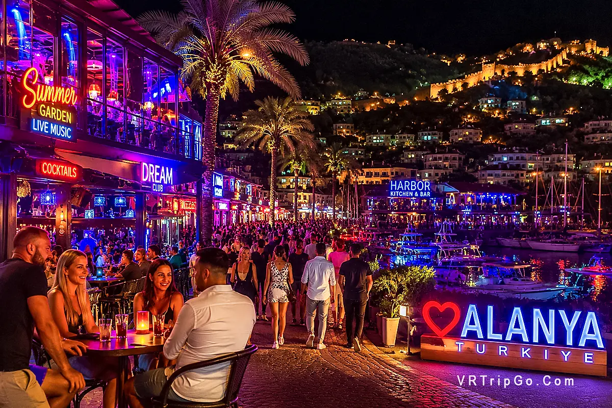 Nightlife in Alanya with vibrant harbor bars, neon lights and crowded promenade, people enjoying nightlife and live music by the sea in Alanya Turkey