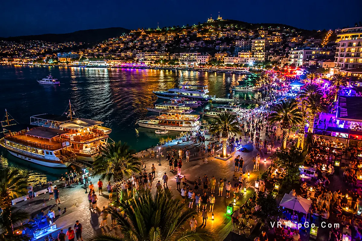 Nightlife in Kusadasi with vibrant bars, marina promenade, luxury yachts and colorful evening lights along the Aegean coast.