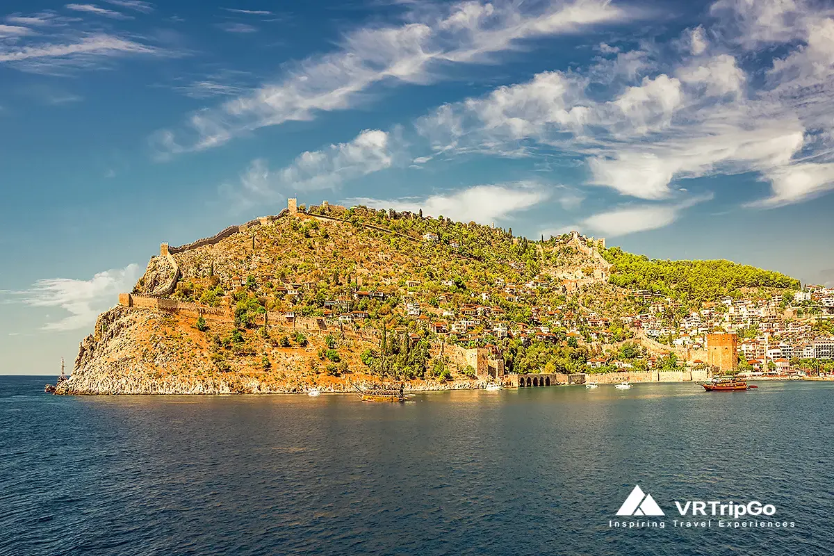 Alanya weather in spring – panoramic view of Alanya Castle on a green hillside with clear blue sky and calm Mediterranean sea