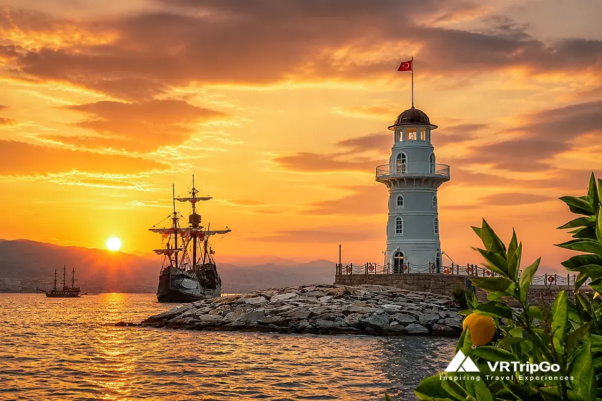 Alanya weather in autumn – lighthouse and sailing ships at warm sunset with golden sky and calm Mediterranean sea