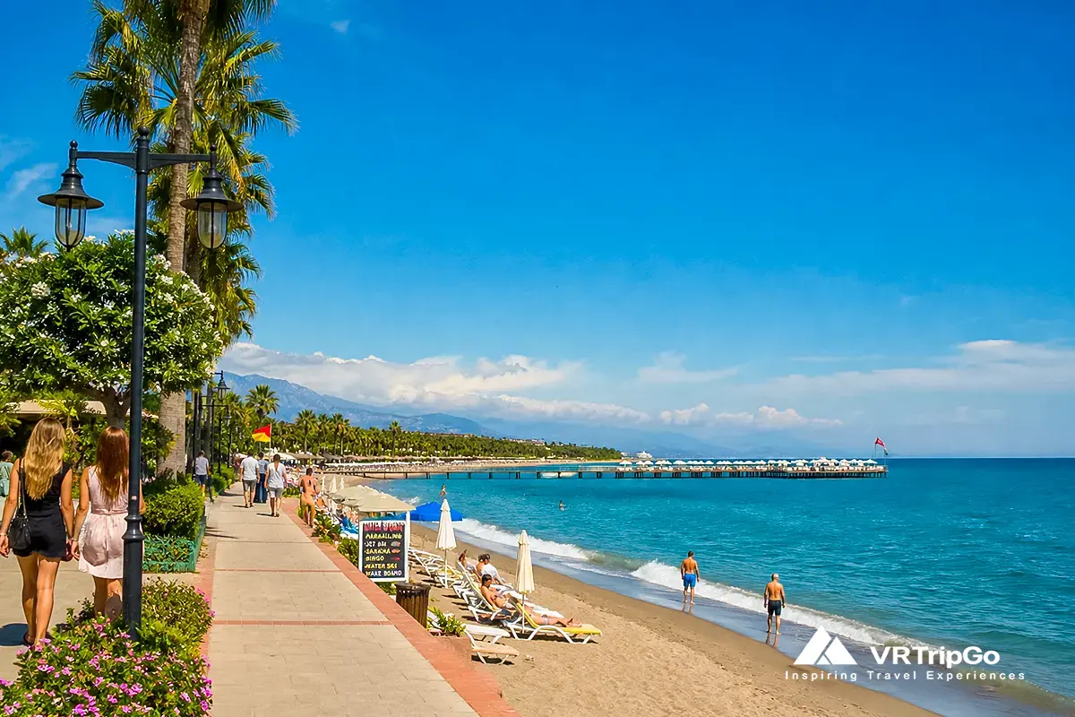 Belek beach in summer weather, hot sunny day, clear blue sky, turquoise sea, tourists relaxing on sun loungers and walking along the shoreline, Antalya Turkey