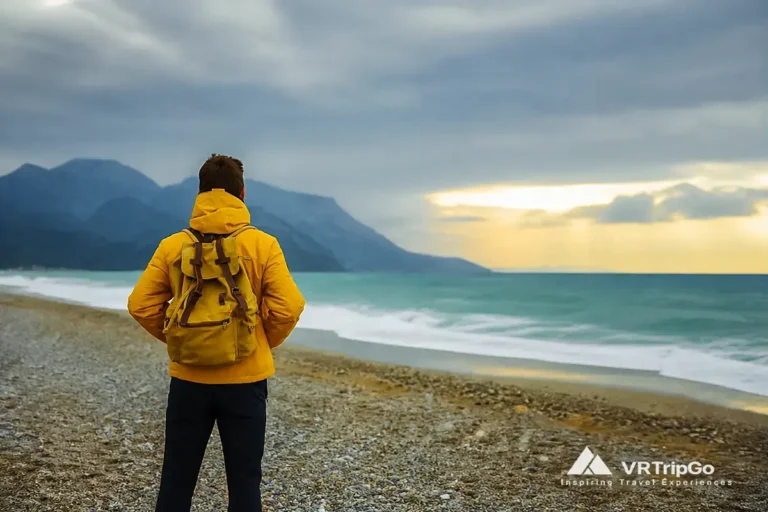 Man standing on Kemer beach with calm sea and mountains during shoulder season, ideal weather for beach holidays in Kemer