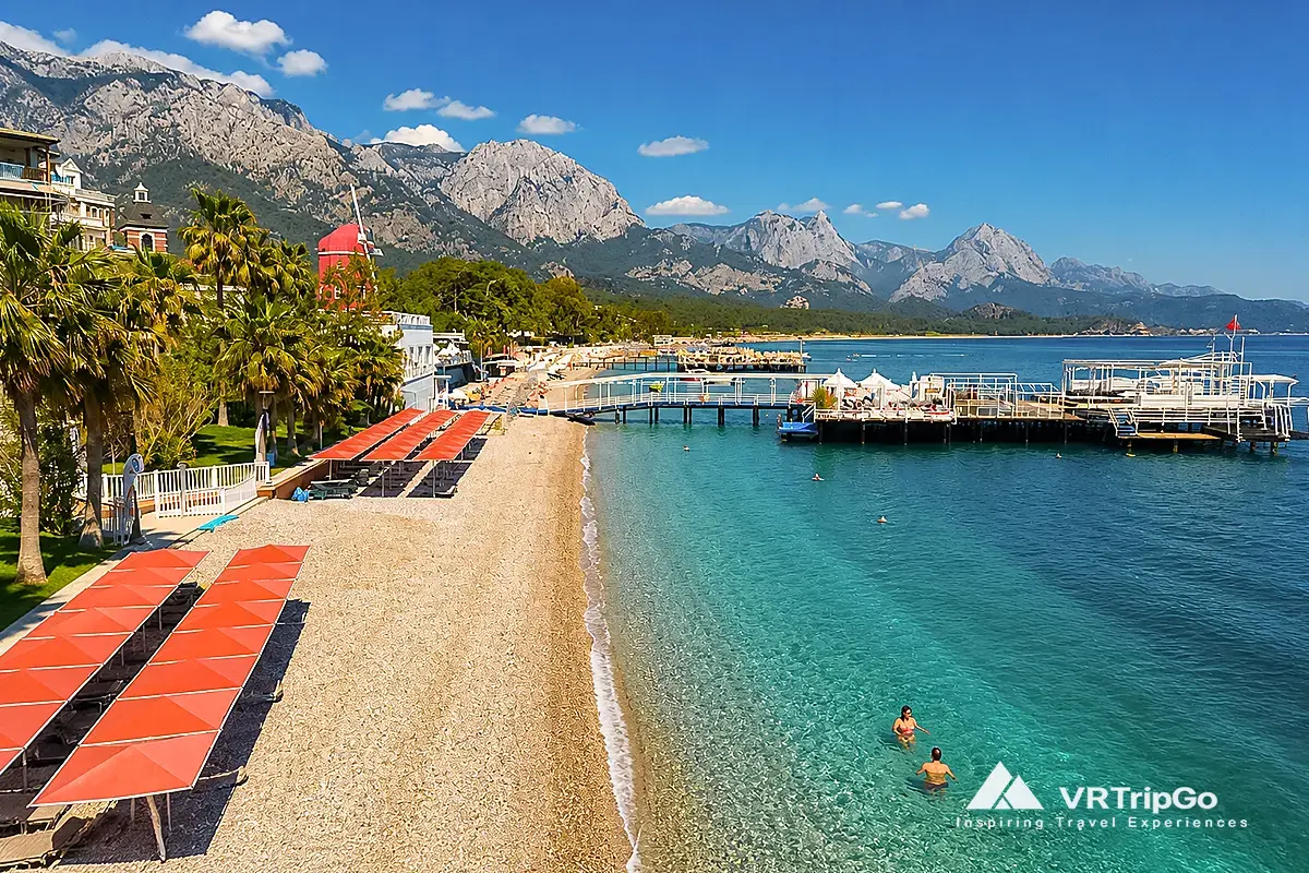Kemer beach with clear turquoise water, swimmers and mountain views in summer, showing best time to visit kemer for beach holidays
