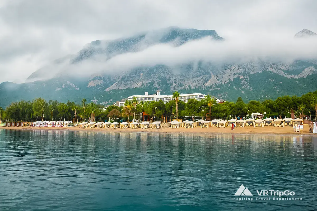Kemer beach with clear turquoise water, swimmers and mountain views in summer, showing best time to visit kemer for beach holidays