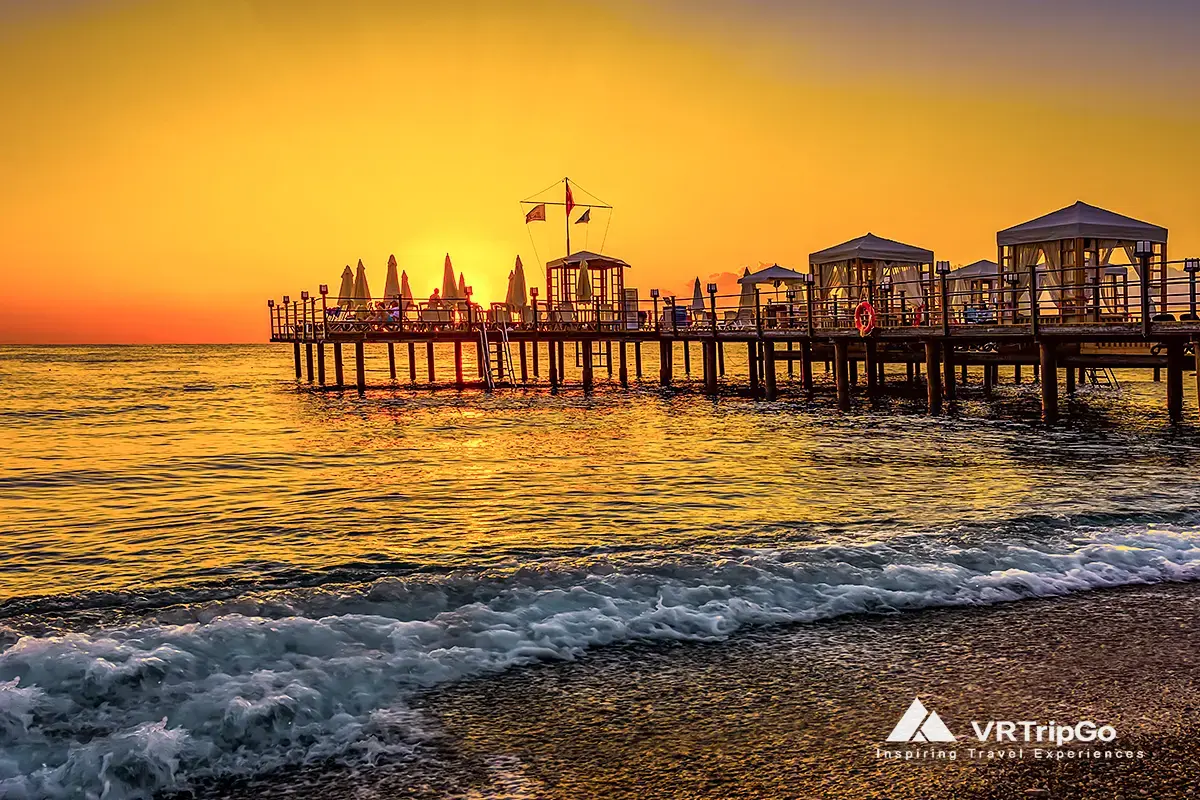 best time to visit kemer for prices, sunset beach pier in Kemer Turkey with golden sky and calm sea waves at evening