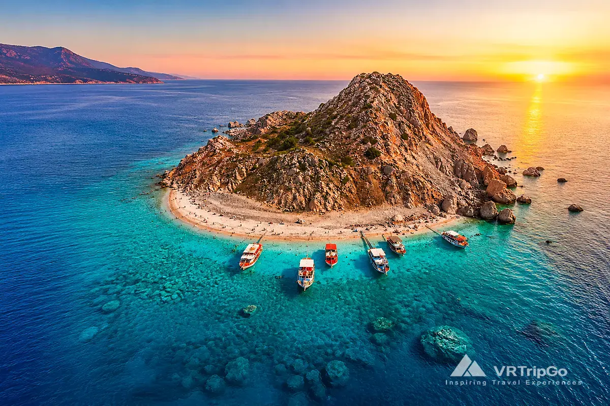 Suluada Island Boat Tour featuring the famous white beach of Suluada, crystal-clear turquoise waters, excursion boats lined along the shore, and breathtaking Mediterranean island scenery at sunset