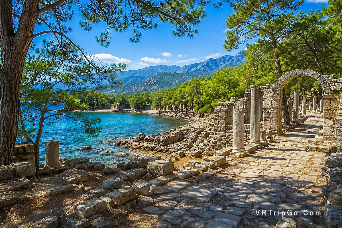 Phaselis Ancient City Tour featuring ancient Roman ruins, historic stone columns, turquoise Mediterranean waters, and breathtaking coastal scenery surrounded by pine forests near Kemer.