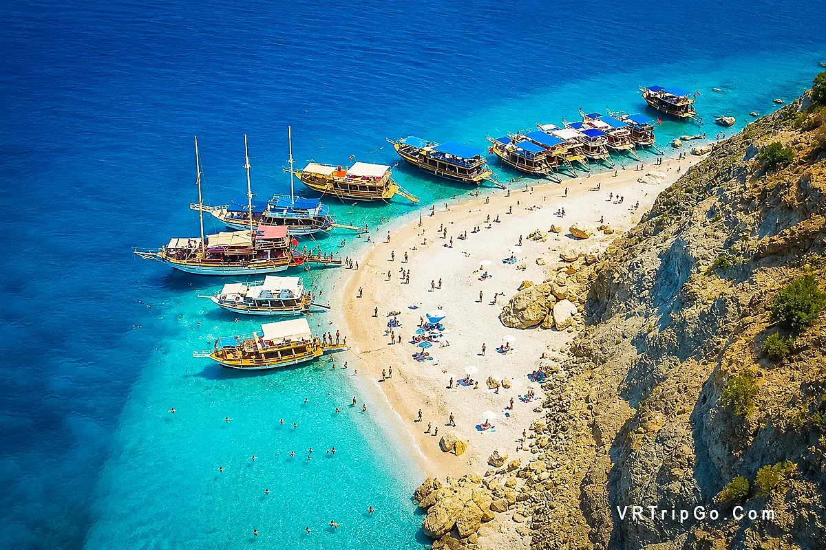 Mediterranean Boat Trip from Belek featuring crystal-clear turquoise waters, traditional boats, a secluded beach, and a stunning Mediterranean coastline.