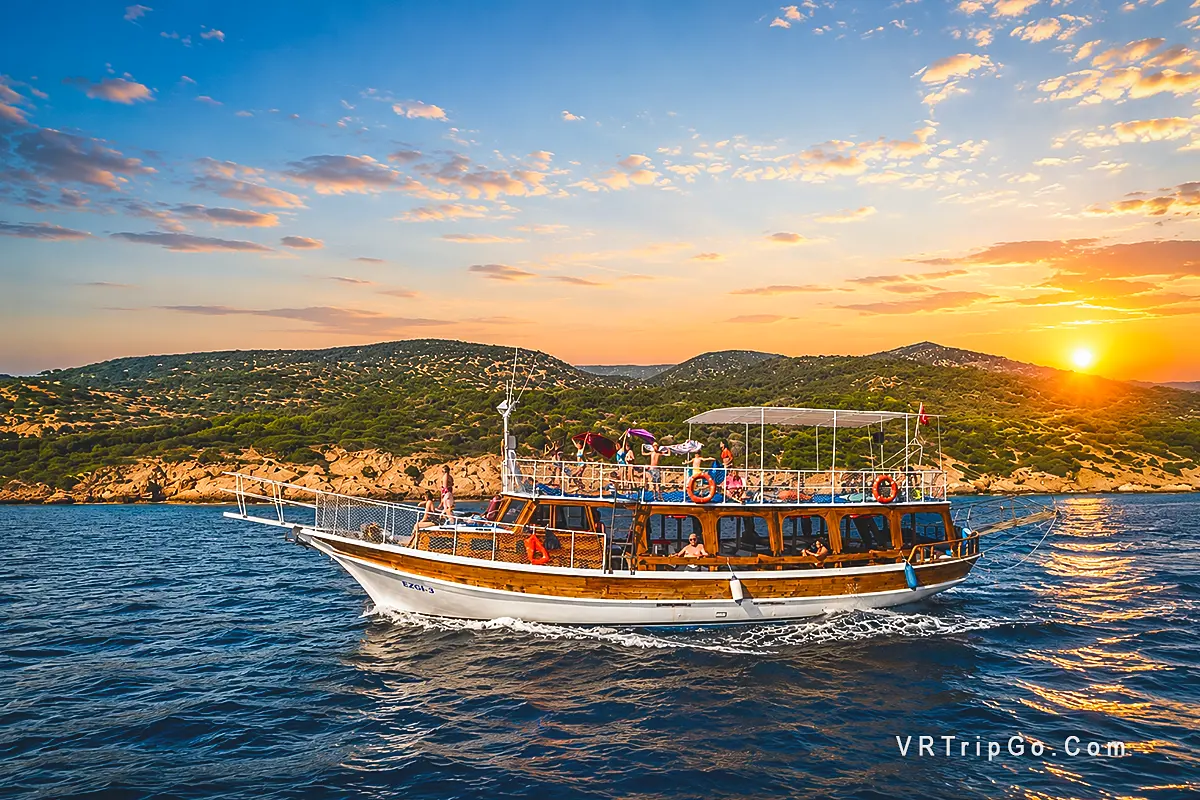 Bodrum Boat Tour featuring a traditional wooden boat cruising along the Bodrum coastline at sunset with crystal-clear Aegean waters and scenic coastal views.