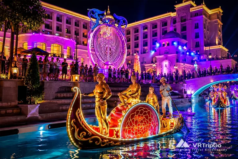 Night show at The Land of Legends in Antalya, featuring illuminated parade boats, golden-costumed performers, colorful lights, and a spectacular canal setting.