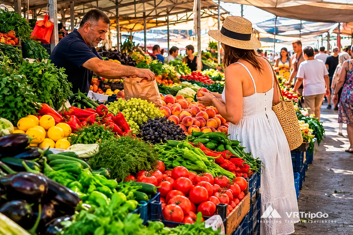 Local vendor selling fresh fruits and vegetables to a woman at Kemer Monday Market, with colorful produce stalls and shoppers in the background.