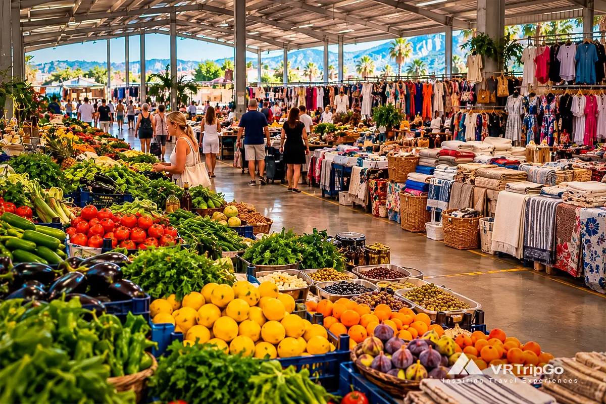 Covered Camyuva Neighborhood Market in Kemer with fresh fruits, vegetables, clothing, household textiles, and shoppers browsing colorful stalls.